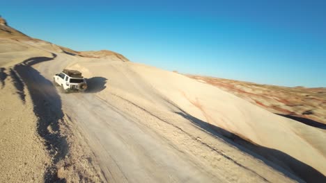 aerial fpv view of white suv driving along path through the bentonite hills in utah