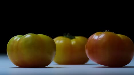 Zeitlupenaufnahme-Von-Zwei-Roten-Roma-Tomaten,-Die-Auf-Drei-Gelben-Geschmackvollen-Tomaten-Auf-Einer-Weißen-Oberfläche-Fallen-Und-Hüpfen