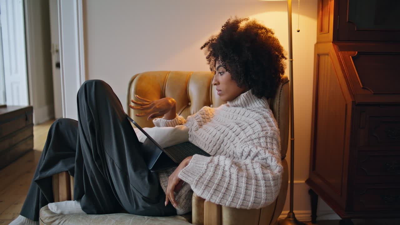 chica tranquila deslizando la pantalla de la casa. morena rizada viendo las noticias de desplazamiento de la pestaña