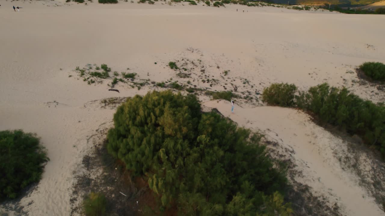 tiro de drone ascendente de una mujer corriendo en tarifa, las vastas dunas de arena de españa
