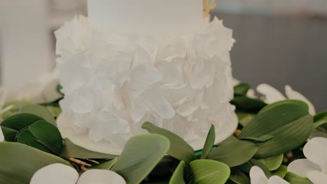 close-up of elegant white cake with floral ruffle design, surrounded by green leaves