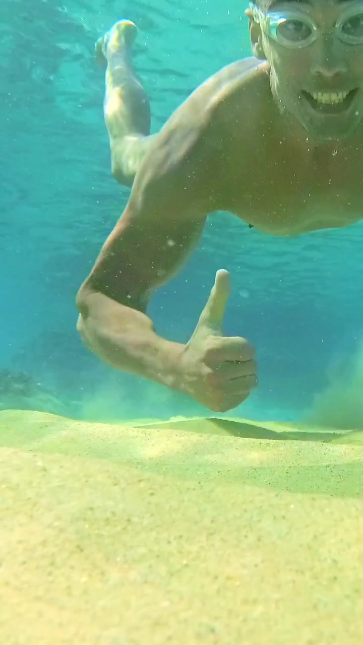 Giovane uomo che nuota sott'acqua verso la fotocamera in Grecia