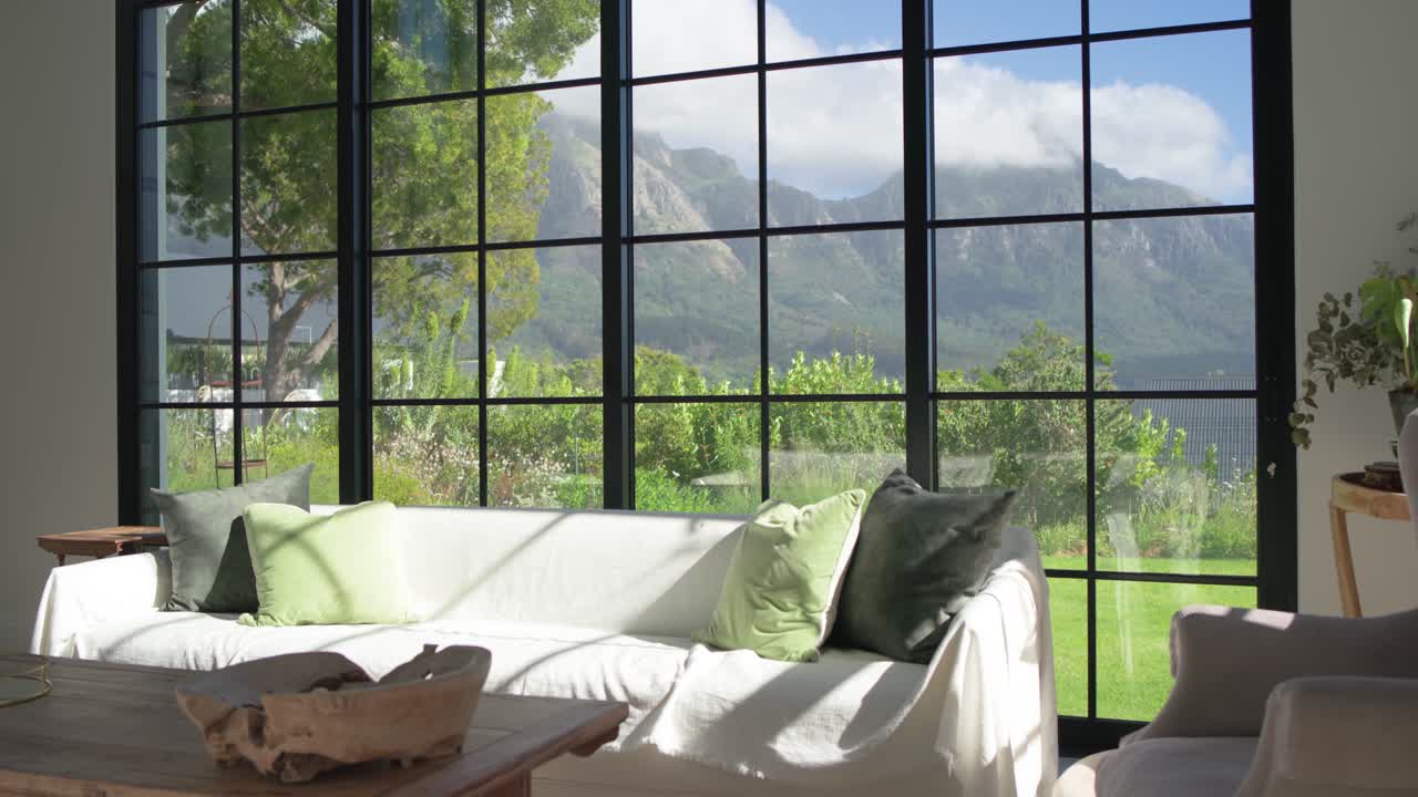 Sofá blanco captando luz en movimiento junto a la ventana mientras la cámara panea hacia la derecha, revelando un sillón.