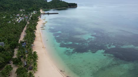 Breathtaking,-Establishing-Overhead-Drone-Shot-of-crystal-clear-ocean-bay-with-shallow-reefs-faced-by-white-sand-beaches-and-dense-jungle-of-Virac,-Catanduanes