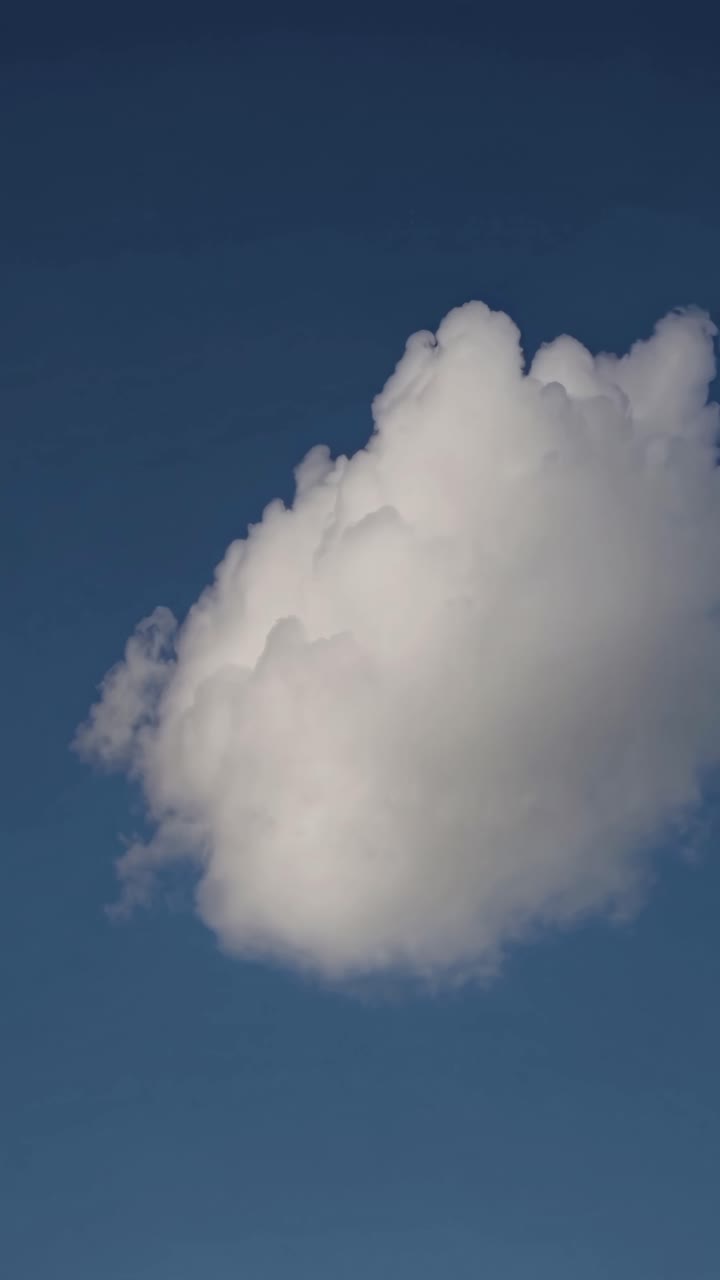 A serene video captures a fluffy white cloud against a deep blue sky, shot from a low angle