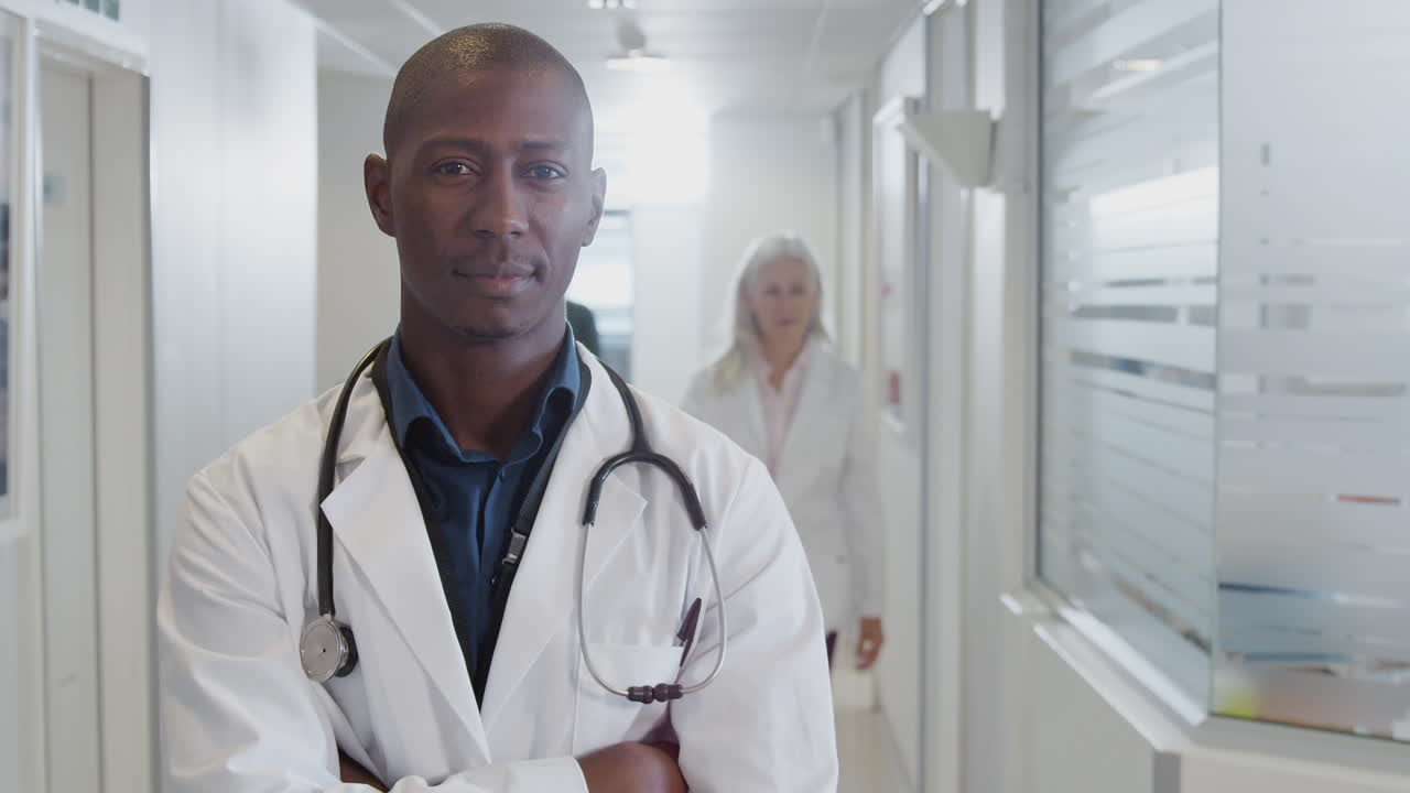 Portrait d'un médecin homme souriant portant une blouse blanche avec un stéthoscope dans un couloir d'hôpital animé