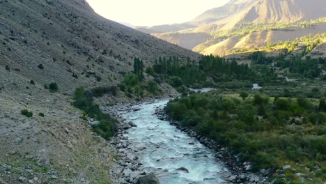 aerial drone of a glacier river flowing through the mountains of astore valley in pakistan during a sunset afternoon in the summer