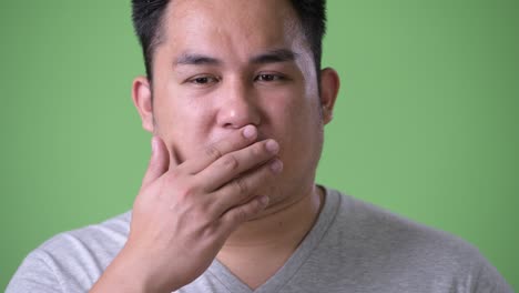 young handsome overweight asian man against green background