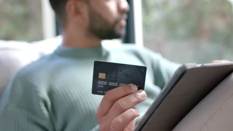 Young-Asian-man-shops-online-using-a-tablet-and-credit-card-at-home