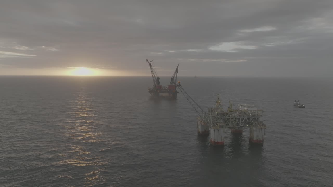 Droneoptagelser af 2 olieplatforme ved solopgang og solnedgang på det åbne hav