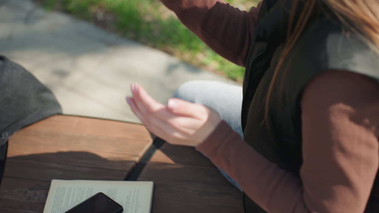 공원에서 추정하는 소녀, 햇빛 아래에서 공부하는 빨간 머리 여성, 피크닉 테이블에서 손으로 셈하는 백인 여성, 노트를 보고 디지털 기기를 고민하는 학생이 있는 밝은 야외 환경