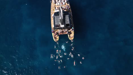 El-Hombre-Salta-Del-Barco-Al-Agua,-Catamarán-En-Agua-De-Mar-Azul,-Hermosa-Bahía-En-Una-Isla,-Tenerife,-Barco,-Verano,-Drone