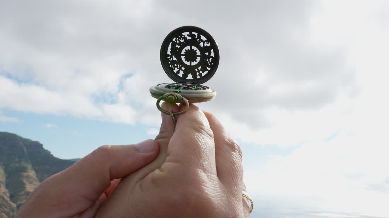 Hands holding and opening compass in mountain landscape
