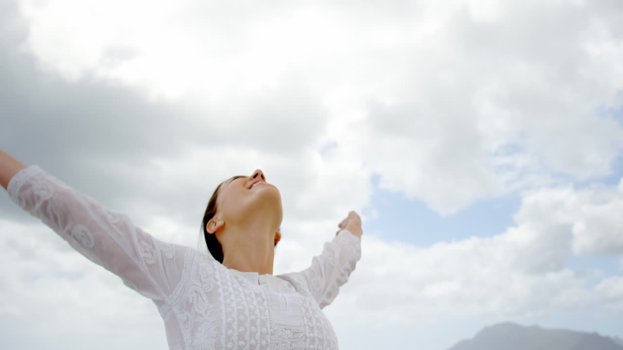 해변 4k에 팔을 펴고 서 있는 젊은 백인 여성의 낮은 각도 뷰