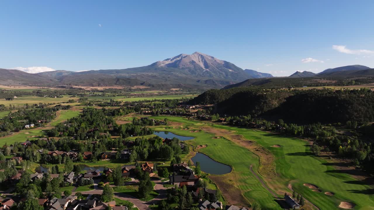 Aerial sweep opens across Carbondale’s golf course, parks and rooftops stretching toward Mount Sopris in soft daylight, pullback establishing