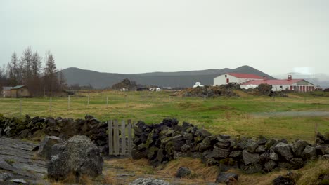 rural icelandic farm with lava rock fence, overcast sky, and distant mountains, static shot