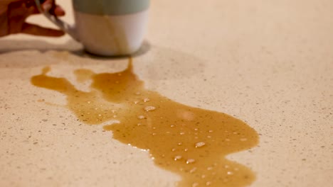 a coffee spill on a countertop is cleaned with a pink cloth. bright lighting highlights the action and environment