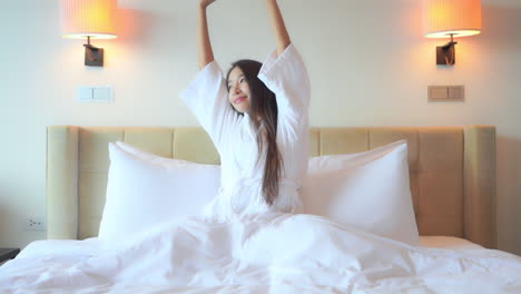 Happy-pretty-asian-female-stretching-hands-in-bed-after-waking-up,-slow-motion
