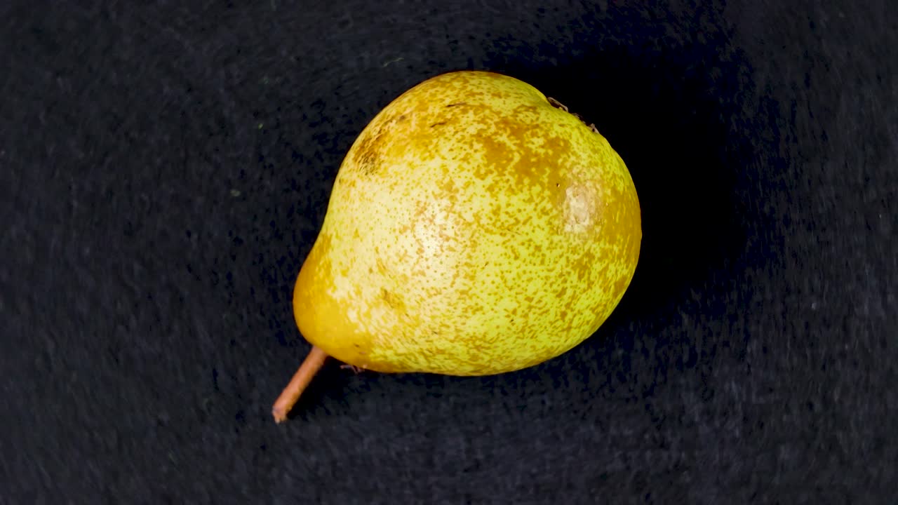 Single yellow pear rotating on a dark black background
