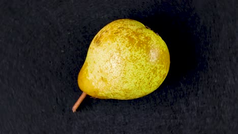 single yellow pear rotating on a dark black background