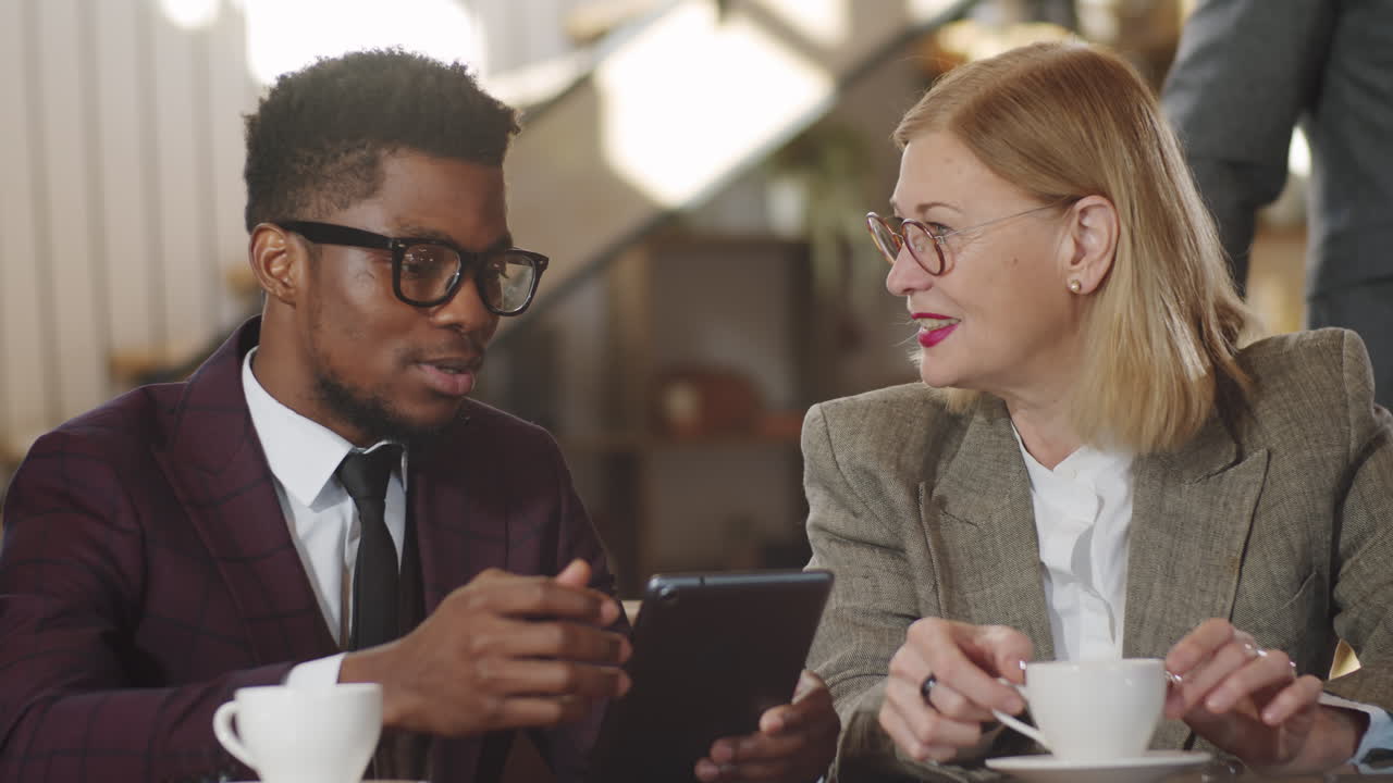 Multiethnic Man and Woman Discussing Business Project on Tablet in Cafe