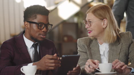 multiethnic man and woman discussing business project on tablet in cafe