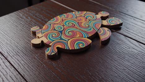 colorful wooden turtle puzzle spinning gently above dark wooden surface, revealing intricate swirling design and delicate craftsmanship of handmade educational toy