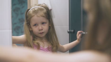 Una-Chica-Feliz-Hace-Muecas-En-El-Espejo-Del-Baño-Luminoso-En-Casa