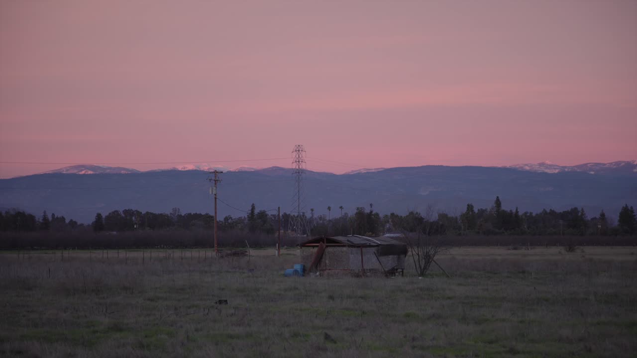 Um céu em tons pastel sobre as montanhas da Sierra Nevada com linhas de energia e um barracão em primeiro plano em Clovis, CA, EUA