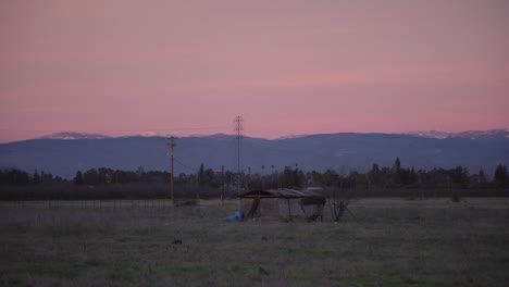 A-pastel-sky-over-the-Sierra-Nevada-mountains-with-power-lines-and-a-shed-in-the-foreground-in-Clovis,-CA,-USA