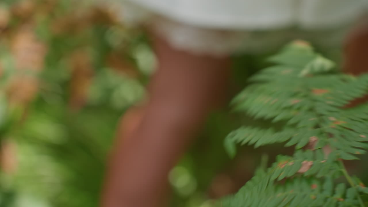 Close up partial view of lady in white gown touching green plant leaf softly then walking away through forest sunlight breeze moving around leaves showing calmness with connection with nature