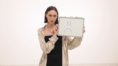 woman holding a whiteboard with a sad face drawn on it