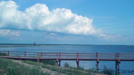 time lapse of beautiful white fast moving puffy cumulus clouds at footbridge path and birdwatching tower at lake liepaja in sunny summer day, wide shot