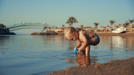 Lustiger-Kleiner-Junge,-Der-Abends-In-Einer-Ruhigen-Meeresbucht-Wasser-Ins-Blaue-Gießt.