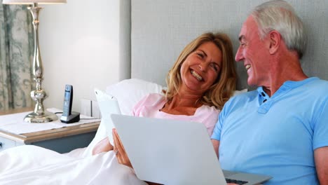 happy senior couple on bed using laptop and digital tablet