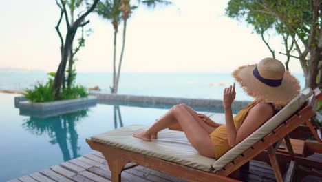 A-lovely-young-woman-looks-out-to-sea-from-the-comfort-of-her-sun-lounger-around-a-resort-swimming-pool