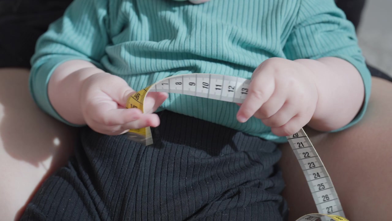 Un bambino tiene un metro a nastro nelle sue manine e ci gioca
