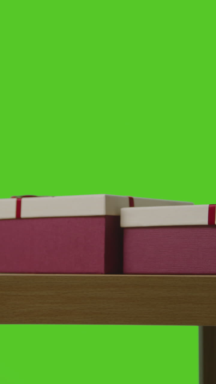 video vertical de un hombre tomando un regalo de una caja envuelta en regalo en la mesa disparado contra una pantalla verde