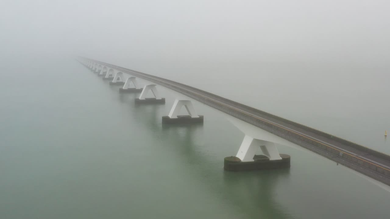 Traffic crossing a long bridge above the sea during fog. Drone shot