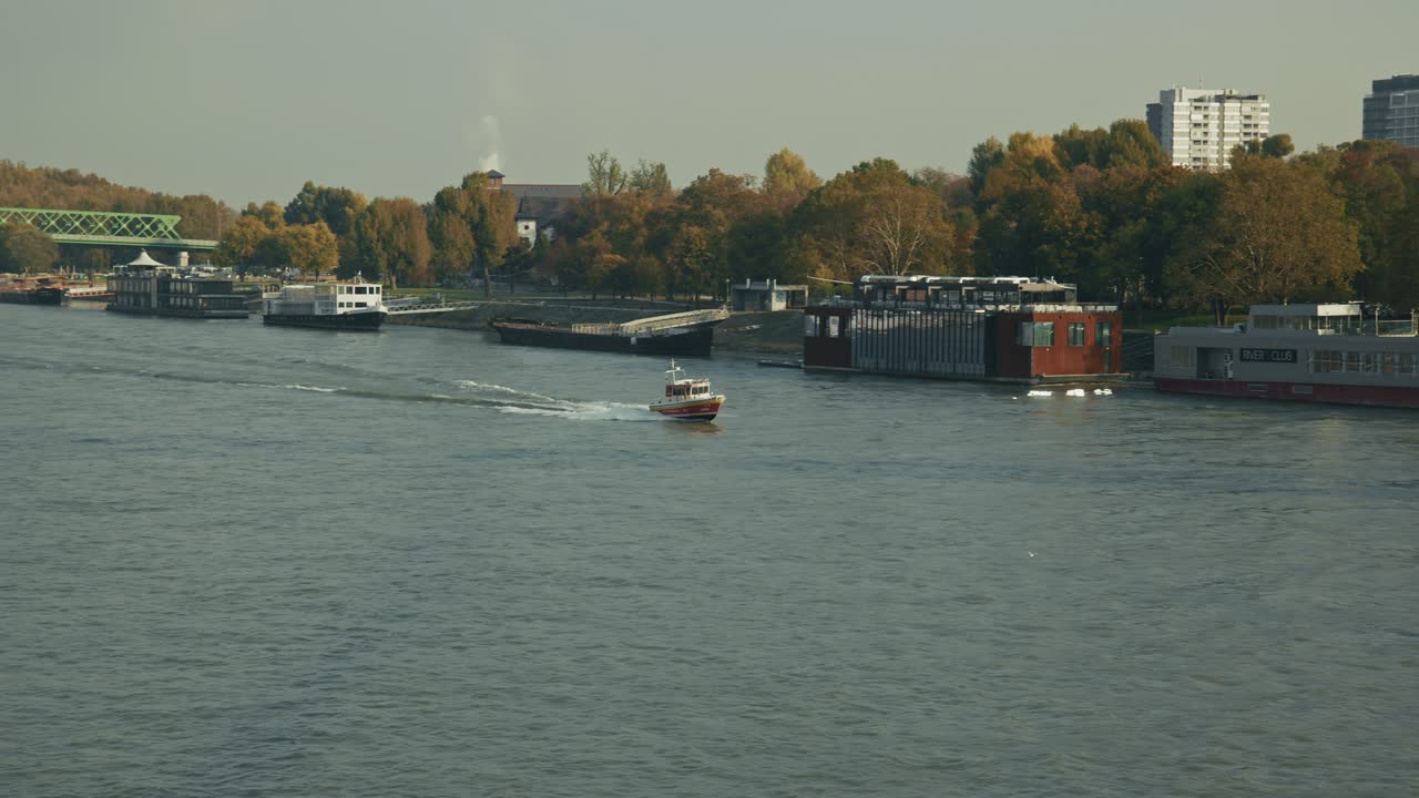 small boat moves along the Danube River in Bratislava with moored ships nearby
