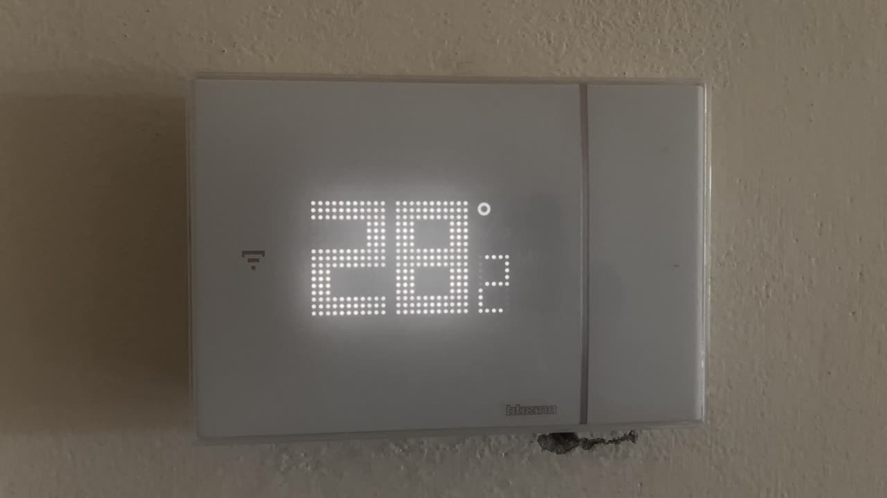 Close-up of a digital thermostat displaying 28°C. Camera tilts down from the wall to the device, concept of summer heat, climate control, and indoor temperature regulation