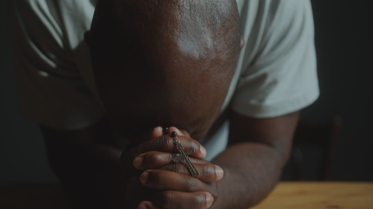 African American Man Holding Cross and Praying Deeply with Bible