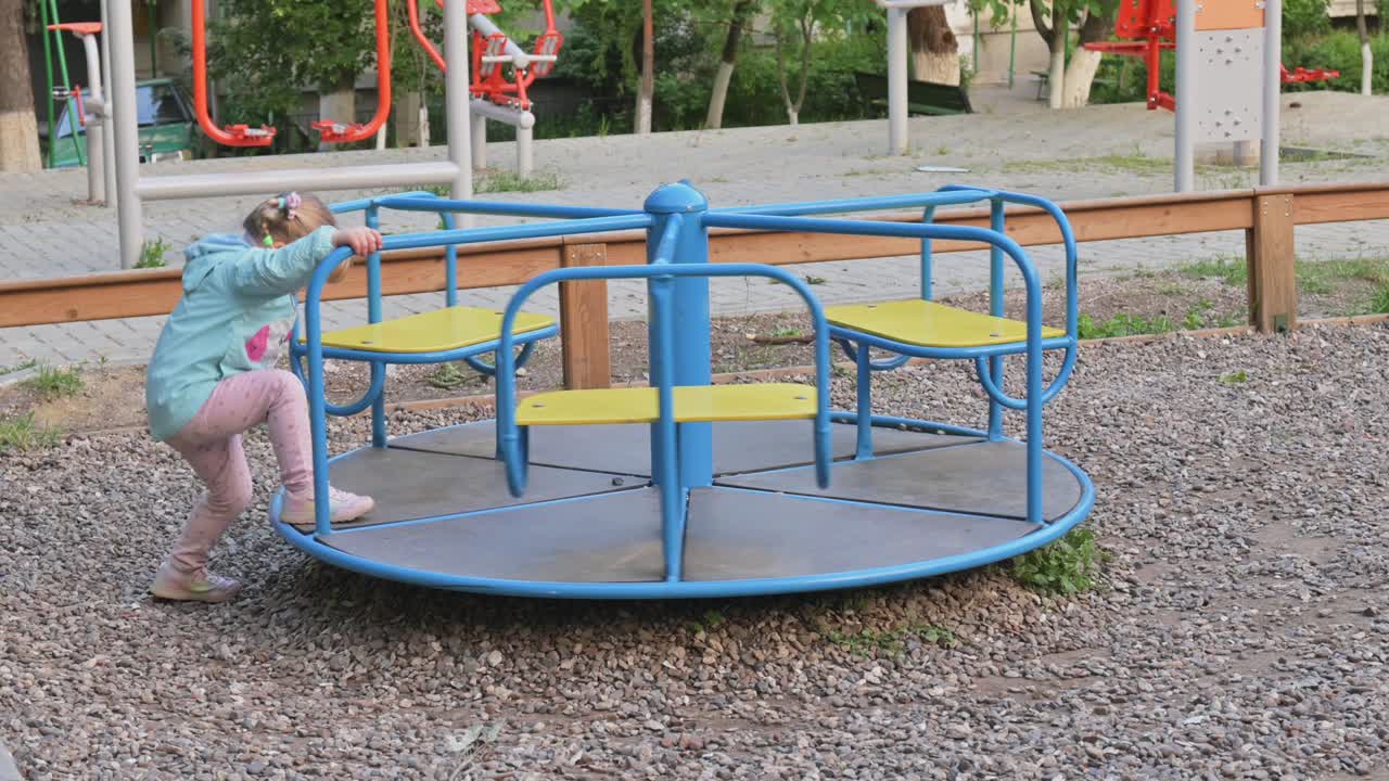 маленькая девочка едет на карусели на детской площадке