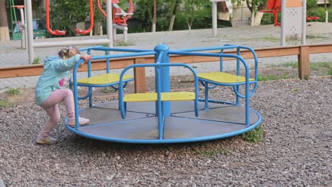 niña pequeña montando el carrusel en el patio de recreo de niños