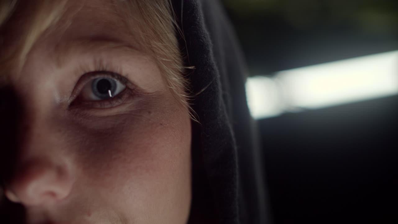 mujer rubia con ojos azules y sudadera con capucha, fondo de tubos de luz blanca, primer plano