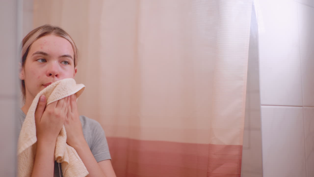Mirror reflecting woman using towel to clean face after washing, focusing on acne and blemishes, skincare hygiene, , refreshing skin, and selfcare moment in bathroom with curtain background