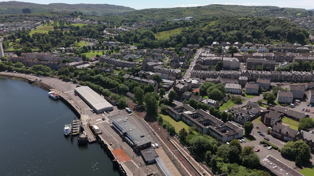 Orbita aerea cinematografica che mostra la stazione ferroviaria di Gourock e le case residenziali lungo la suggestiva costa scozzese. Vista dall'alto delle infrastrutture di trasporto e della pianificazione urbana.