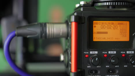 a presenter on green screen recording into an audio field recorder in a video production studio with volume displayed on a digital level display