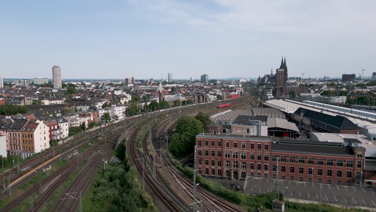 un vuelo de cámara altísimo que revela la catedral y la estación principal de tren con la plataforma de vía vacía de colonia, alemania, en un día de verano.
