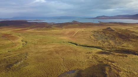 Drone-backing-up-and-rising-to-reveal-farmland,-lake-and-mountains-in-the-distance